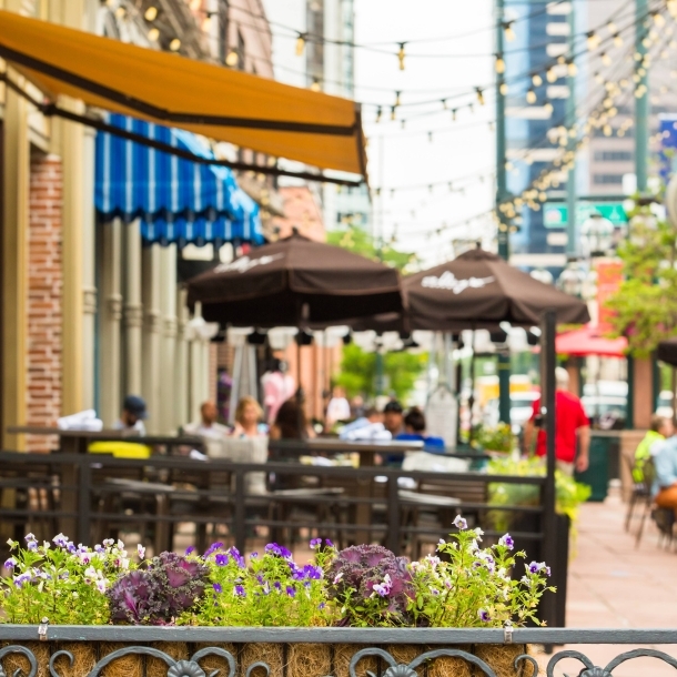 Outdoor café with tables, umbrellas, and potted flowers on a city street.
