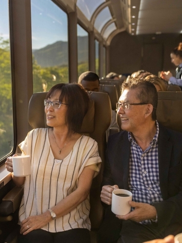 Couple on a train enjoying drinks, scenic view outside.
